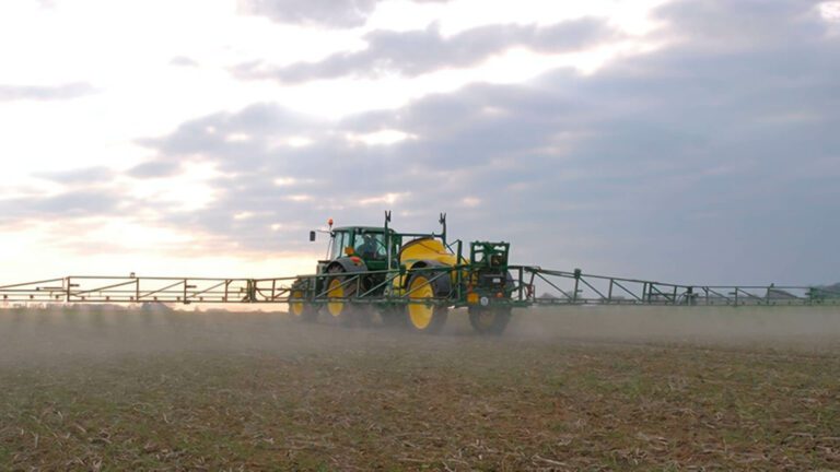 Trator com barra de pulverização aplicando defensivo no campo