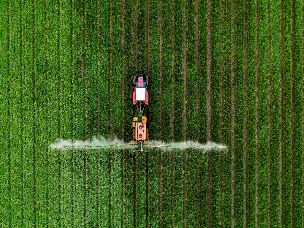 Trator aplicando fertilizante em um vasto campo verde, visto de cima