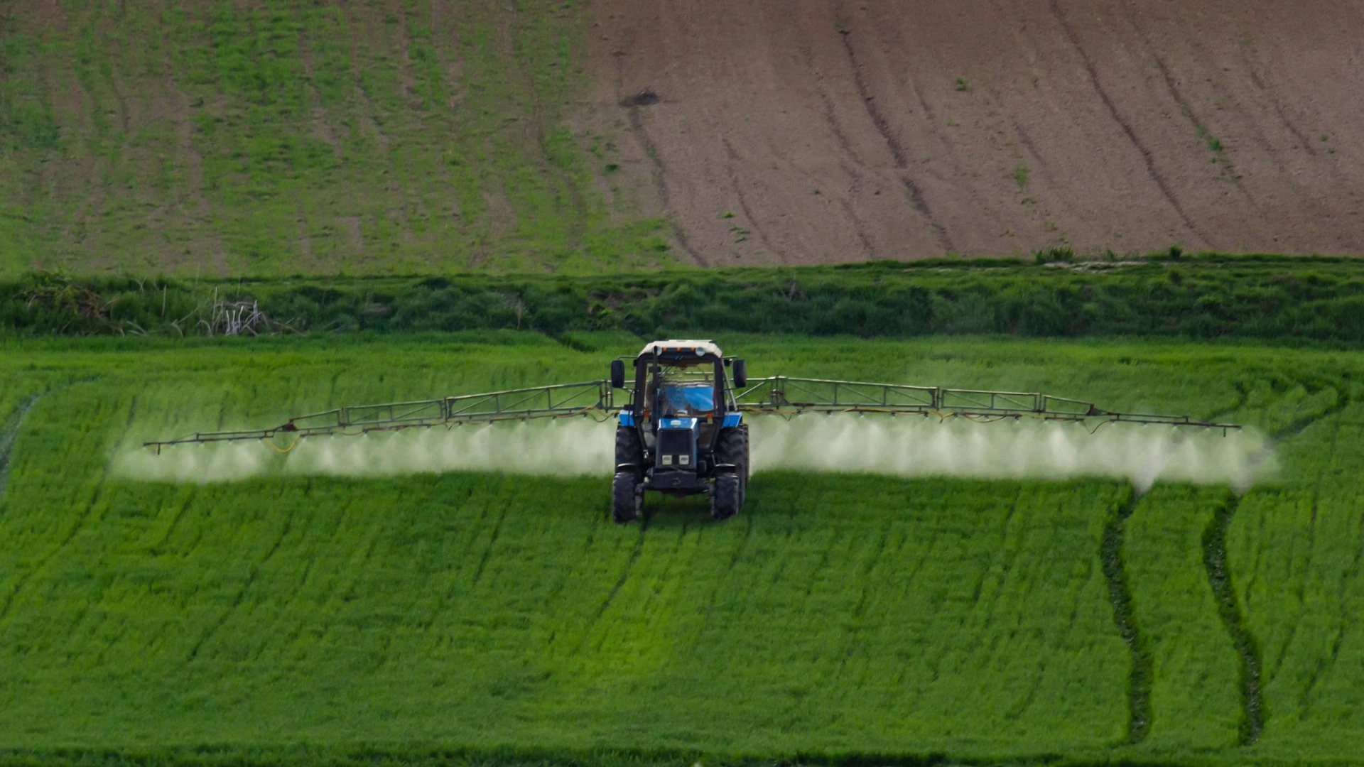 Vista aérea do trator de pulverização de cultura em campos agrícolas verdes.