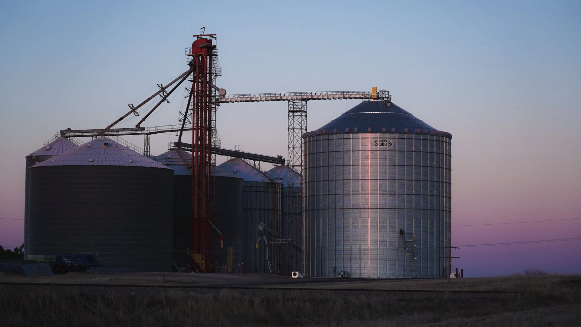 Um pôr do sol rosa se transforma em crepúsculo atrás de grandes celeiros.