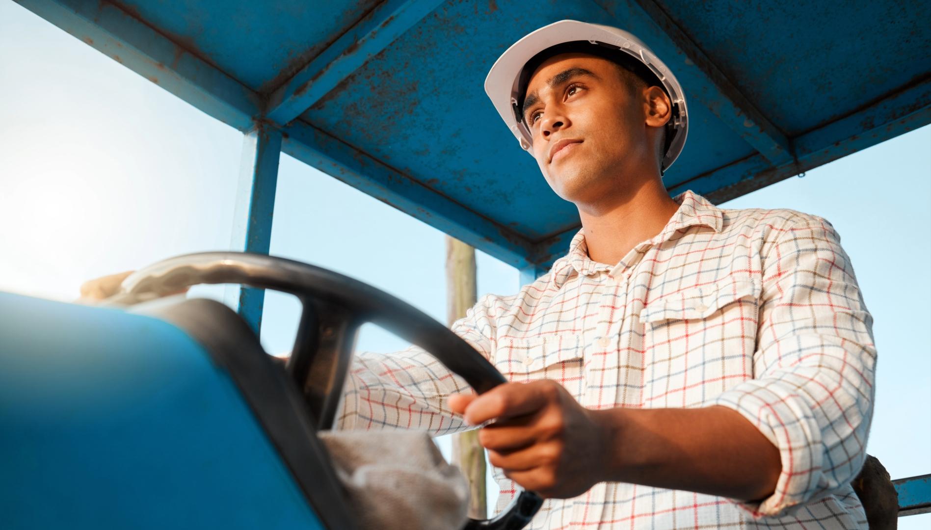 Close de produtor rural conduzindo trator durante atividades de manejo e colheita na lavoura.
