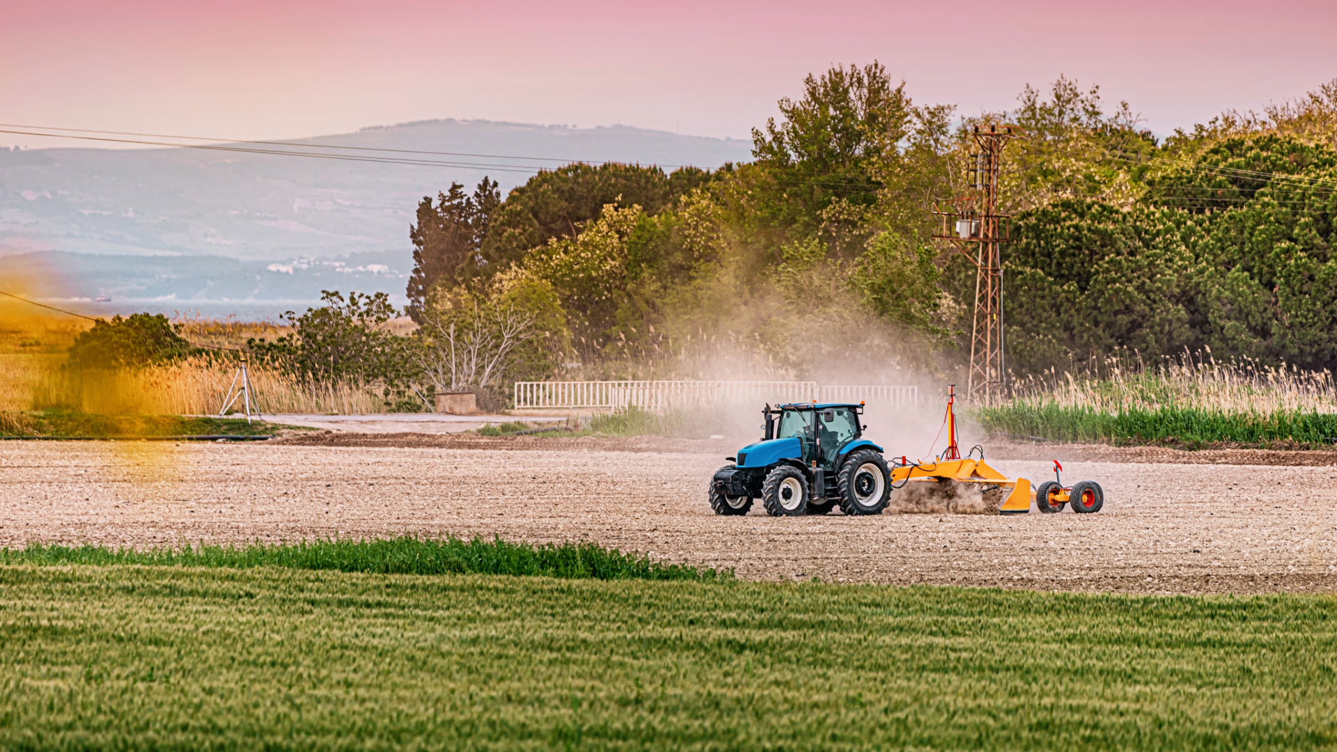 Trator trabalhando em campo aberto durante o dia com restos de plantio sobre o solo.