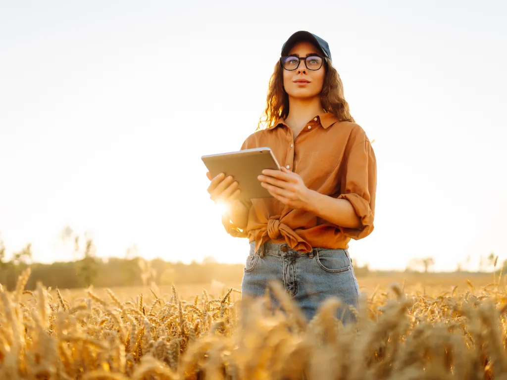 Uma agricultora se posiciona em um campo de trigo, segurando um tablet