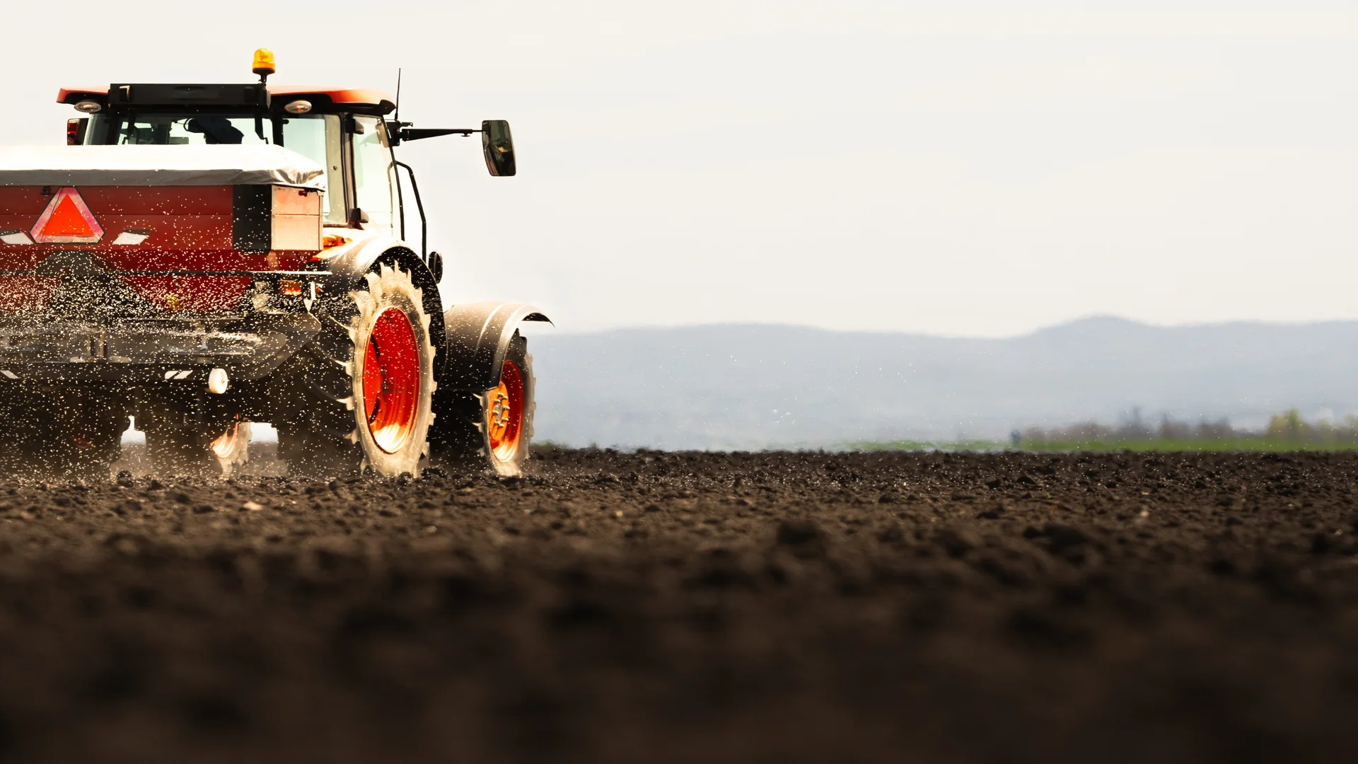 Trator espalhando fertilizantes no campo.