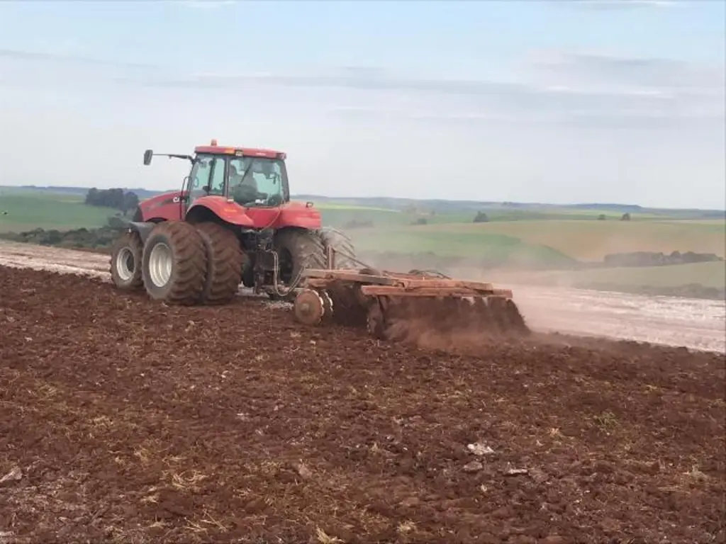Trator compactando a terra com céu azul entre nuvens ao fundo